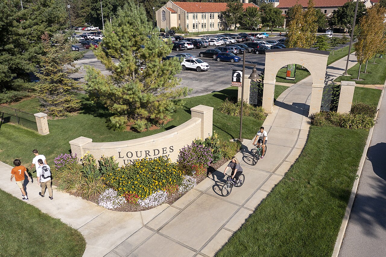 Students walk and cycle past the Lourdes University entrance sign in Sylvania, Ohio