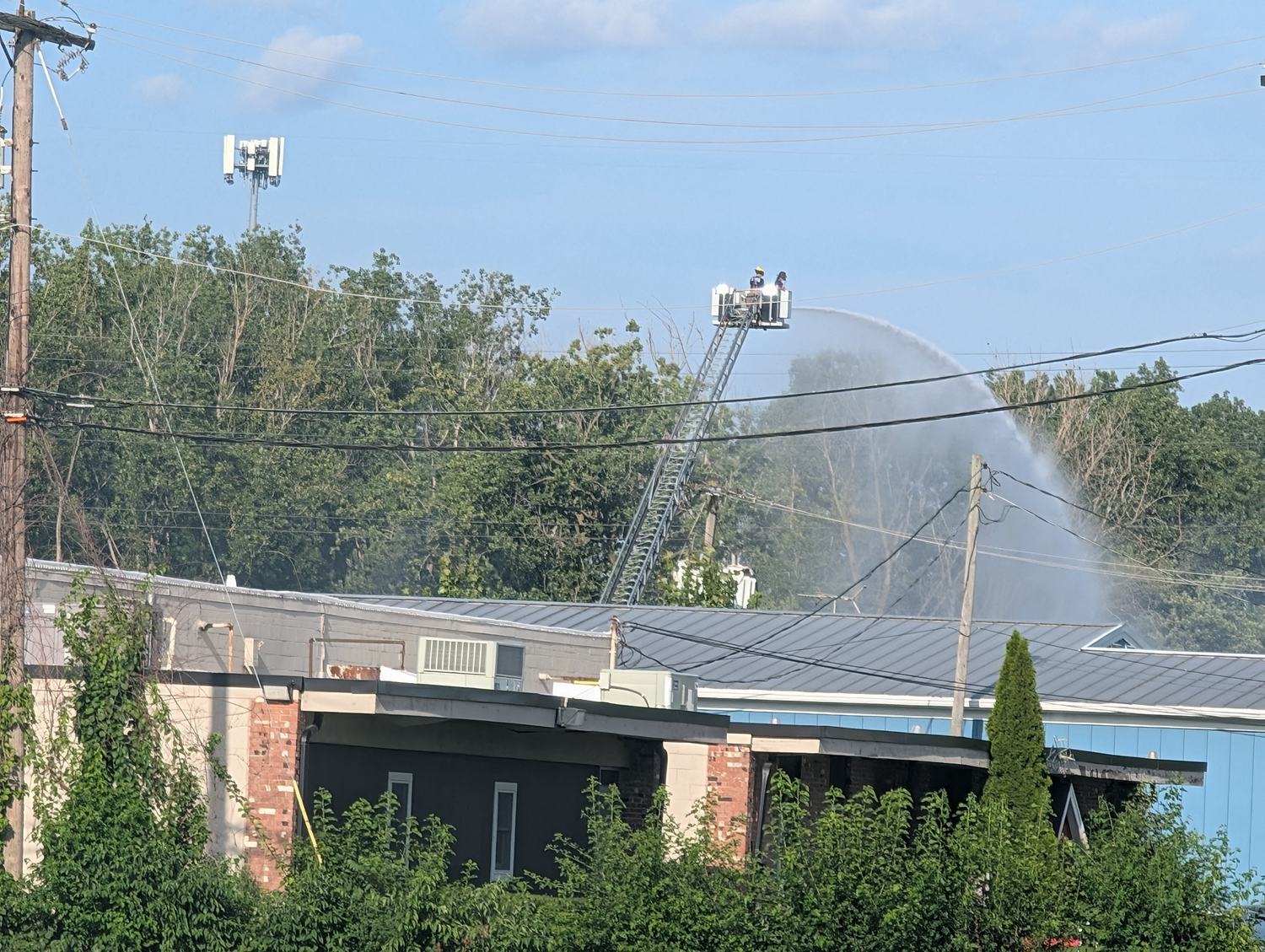 A Toledo firefighter on an aerial ladder pours an elevated stream of water onto the low commercial building at Brent Industries under a clear sky, roughly twelve hours after the blast / Un bombero de Toledo en una escalera a&eacute;rea lanza un chorro de agua sobre el edificio comercial de Brent Industries bajo un cielo despejado, unas doce horas despu&eacute;s de la explosi&oacute;n