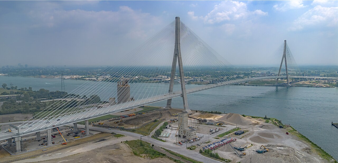 Aerial view of the Gordie Howe International Bridge over the Detroit River, two towers strung with white cables above an empty deck / Vista aerea del puente internacional Gordie Howe sobre el rio Detroit, dos torres con cables blancos sobre una calzada vacia