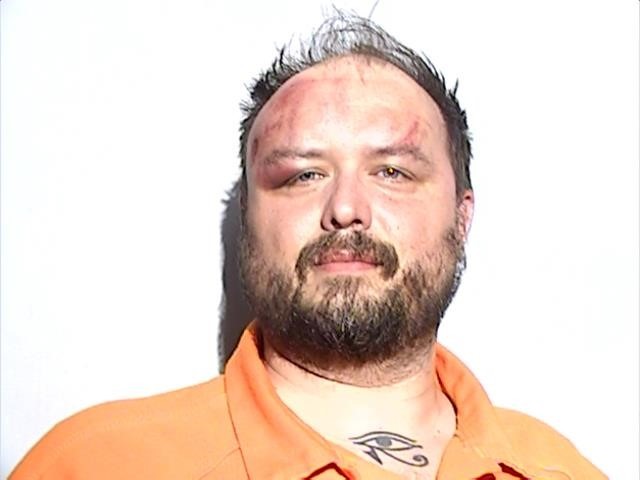 Booking photograph of Matthew Exton at the Lucas County Corrections Center: a bearded man in an orange jail shirt, with a swollen left eye and a scrape across his forehead. / Fotografía de ingreso de Matthew Exton en el centro correccional del condado de Lucas: un hombre con barba, camisa naranja de la cárcel, el ojo izquierdo hinchado y un raspón en la frente.
